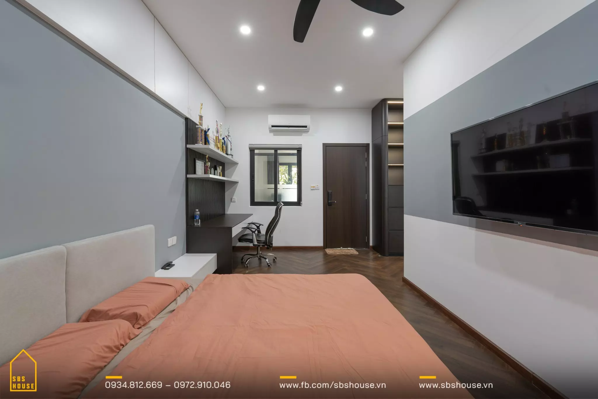 Phòng ngủ với thiết kế nội thất đơn giản và hiện đại. Trung tâm của căn phòng là một chiếc giường đôi với chăn ga màu cam nhạt, đầu giường màu be. 